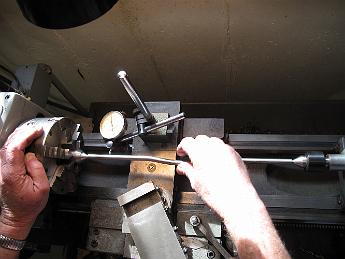 TumblingShaftFinishing31Jan09 004 31-Jan-09 With the shaft held between centers (we had drilled center holes in the ends before bending), we use a dial indicator to measure the total indicated runout after the bending operation.  The stresses of the cold-formed bend caused the ends to move around, with a very large runout next to the bend point. We focused on getting each end to be within a thou of each other, around the area held in the pillow block. With this we are confident the tumbler shaft will rotate without binding.
