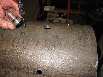 SmokeboxShellSaddleDrilling28Feb08 007 Two holes down, 22 more to go.  Here's how it went: Using the pointed wiggler, line the punch point on the shell up under the spindle. After checking the front and side alignment with a magnifying glass, bolt the shell down and check the alignment again.  We found the shell moved slightly each time we tightened the hold-down screws.  Keep adjusting until things are tight but still true to the punch mark. Center drill a hole, Tap drill al the way through, Tap for for a 10-32. I wanted the extra security of a threaded hole in this nice thick smokebox shell instead of just a through hole nut and bolt assembly.  After that hole is done, loosen the clamps, rotate the shell until the next punch mark is on top and repeat: wiggler, center drill, tap drill, tap.